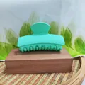 Macro view of a matte mint green rectangular hair claw clip on a wooden block - Green
