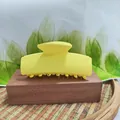 Close-up of a vibrant yellow rectangular matte hair claw clip on a wooden stand. - Yellow