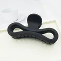Detailed view of a large matte black bow-shaped hair claw clip placed on a white tray - Black