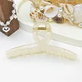 Detail view of a large cream-colored jelly hair claw clip with an elegant ribbon-cross design - White