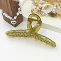 Close-up detail of a large amber jelly hair claw clip with twisted ribbon styling. - Green