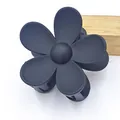 Close-up of a matte black five-petal flower hair claw clip presented on a wooden prop - Black