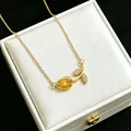 Close-up of elegant gold tulip necklace with yellow gemstone and paved leaves. - Yellow