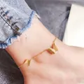 Gros plan sur une élégante chevillère papillon dorée en acier titane portée à la cheville - Style Petit et Grand Papillon (270) / Or