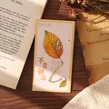 Elegant leaf shaped metal bookmark with gold gradient on vintage book background - Autumn Gradient Leaf
