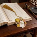 Detailed view of a metal cat bookmark with sunflowers and a golden tassel on a book - Style A (Cat with Sunflowers) / Gold/White