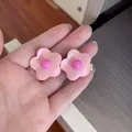 Detailed close-up view of glossy pink candy-colored flower hair clips held in hand - Flower / Pink
