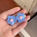Close-up macro view of cute blue flower hair clips with pink centers held in a hand - Flower / Blue