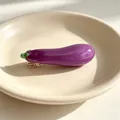 Macro view of a realistic glossy purple eggplant hair clip resting on a beige ceramic plate - Eggplant