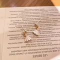 Primer plano de pendientes de bádminton con esmalte blanco y acabado dorado - Volante de Bádminton Blanco (Pendientes de Botón)