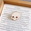 Close-up of a cute white skull enamel pin with rose gold outlines in a wooden tray - Skull