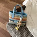 Handgewebte Strohtasche mit Regenbogenstreifen, hellblauen Griffen und Blumenanhänger. - Handgewebt (YM0193) / Blau