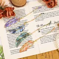 Set of creative metal feather bookmarks with delicate chains on an open vintage book - Emerald and Amethyst and Sun and Lapis