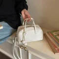 Elegant white pebbled leather Boston handbag with woven edges and decorative ball charms - Off White
