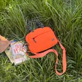 Vibrant orange outdoor travel crossbody bag with black braided rope handle on grass - Small Orange