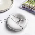 Elegante zilveren slangenschakelketting gestrikt op een witte keramische sieradenschaal - Zilveren Strik Ketting (86431)