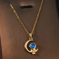 Detail view of a golden astronaut and crescent moon pendant with a blue gem center. - Dreamy Moon Astronaut