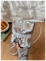 Primo piano di una mano che tiene una borsa per cellulare ricamata azzurra con fiori - Grigio