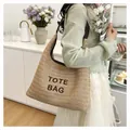 Large hand-woven straw tote bag carried on the shoulder in a cozy cafe setting - Style 1 (Letter Embroidery) / Coffee