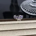 Detailansicht eines silberfarbenen Schleifenrings mit lila Edelsteinen auf Schmucktablett - Violetter Pave-Edelstein-Schleifenstil (Stil 14) / Silber