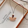 Macro view of a fan-shaped woven pendant necklace on a rustic wooden tray. - Woven Fan Style (X2280E)