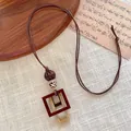 Close-up of geometric wooden square pendant on a brown braided long cord necklace - Nested Rectangular Frame Style (C)
