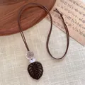Macro detail of the dark brown wooden monstera leaf pendant on a brown woven cord - Hollow Leaf Style (A)