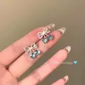 Macro view of sparkling blue heart zirconia earrings with delicate lace bows and pearls. - Bowknot Heart Style (E7115 Silver) / Silver