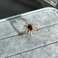 Close-up of elegant flower ring with oval garnet red gemstone in blue box - No. 33 Open Ring