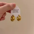 Close-up detail of brushed golden hoop earrings featuring a 925 silver hallmark card - A1970 Matte Gold