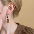 Macro detail of stylish Maillard style amber resin pendant earring on model's ear - Amber Rectangular Resin with Tiger Eye Bead (A2734)