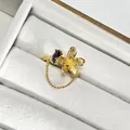 Primer plano detallado de un anillo de flor dorada con gema púrpura y cadena fina. - Anillo Cepillado Borla Gema Púrpura Flor (69815477)