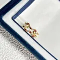 Nahaufnahme eines goldenen Rings mit roten und weißen Zirkonia in einer blauen Box - Einstellbar Offen / Rot & Weiß Edelstein Wellenstil (7号)