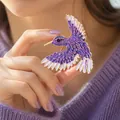 Exquisite purple glitter hummingbird brooch with golden details held by model for display - Purple Spreading Wing Bird / Purple