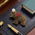 Vintage gouden olifant broche met rode strass steentjes en parel op zwart leer achtergrond. - Antiek Goud Olifant