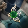 Elegante broche de pez tropical con cristal verde y acabados dorados sobre tela azul - Estilo Pez Tropical (Pez Dorado Mate)