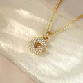 Close-up of a gold-plated letter G pendant necklace fully paved with sparkling crystals. - Letter G / Champagne Gold