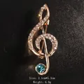 Elegant gold-toned music note brooch with sparkling rhinestones and blue accent gem. - Gold/Sea Blue