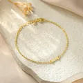 Close-up of golden titanium steel bracelet with letter I charm on textured white stone - Letter I Style / Gold
