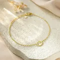 Close-up of minimalist gold titanium steel bracelet with hollow circular charm. - Letter O Style / Gold