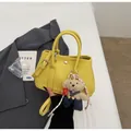 Stylish yellow textured leather handbag with a cute teddy bear charm held by hand - With Pendant / Yellow