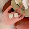 Gros plan détaillé d'élégantes boucles d'oreilles fleurs blanches superposées en main. - Style Fleur 3D Blanche (A1421) / Blanc