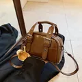 Vintage brown glossy synthetic leather handbag with baseball charm and buckle straps. - With Pendant / Brown