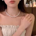 Elegant round pink luster pearl necklace and matching ring set worn by a model in warm light - 12mm Pearl Style (X1312) / Gold