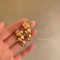 Nahaufnahme von goldenen Ginkgoblatt-Ohrhängern in einer Hand - Ginkgoblatt Quasten Stil (A2188) / Gold