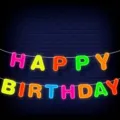 Colorful neon HAPPY BIRTHDAY banner hanging against a dark blue brick wall background. - Neon Happy Birthday Banner