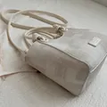 Close-up detail of a minimalist beige bucket bag featuring textured fabric and knotted handles - Without Pendant / White