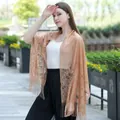 Elegant tan lace shawl with tassel fringes worn by a model in an outdoor setting - Camel