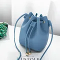 Blue pebbled leather drawstring bucket bag with gold accents in a lifestyle setting. - Blue