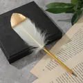 Primo piano di una penna piuma bianca con punta dorata e fusto in metallo dorato. - Avorio